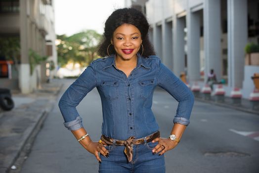 Young happy and free woman standing on the street posing with her hand on her hip and looking at the camera