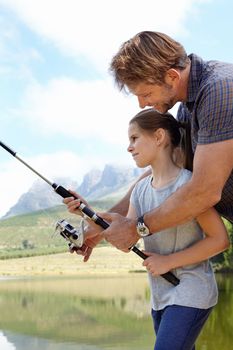 Weve got one. a father showing his daughter how to fish outdoors