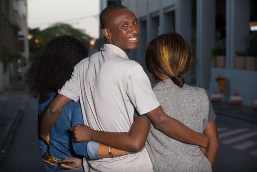 three friends or lovers walking together outdoors.Young man holding women by the waist turns his head to the camera and smiles
