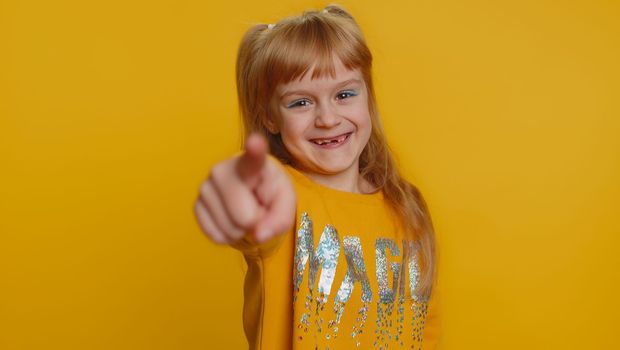 Amused young preteen child girl kid pointing finger to camera, laughing out loud, taunting making fun of ridiculous appearance, funny joke. Little toddler children isolated alone on yellow background