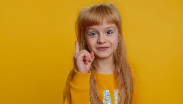 Young preteen child girl kid shakes finger and saying no, be careful, scolding and giving advice to avoid danger mistake, disapproval sign. Little toddler children alone on studio yellow background