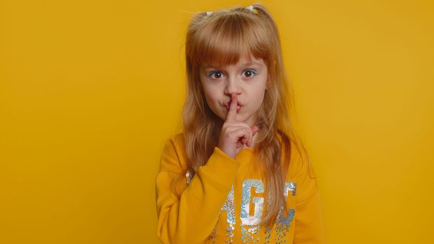 Shh be quiet please. Preteen child girl kid presses index finger to lips makes silence hush gesture sign do not tells gossip secret. Little toddler children isolated alone on studio yellow background