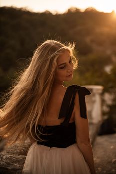 Blonde long hair, nature summer happy adult girl with long blond hair developing in the wind in nature. Dressed in a black top, white skirt