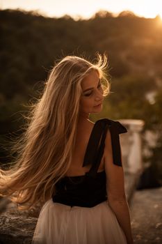 Blonde long hair, nature summer happy adult girl with long blond hair developing in the wind in nature. Dressed in a black top, white skirt