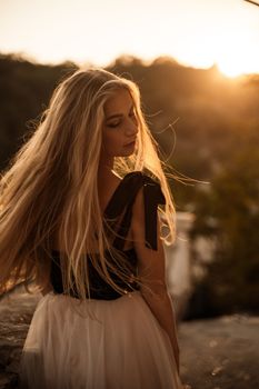 Blonde long hair, nature summer happy adult girl with long blond hair developing in the wind in nature. Dressed in a black top, white skirt