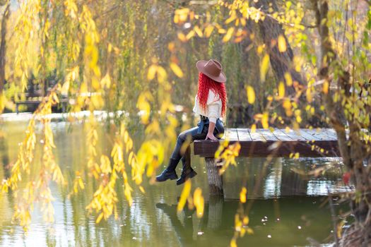 Autumn lake woman. She sits by a pond on a wooden pier in autumn and admires nature. The concept of tourism, weekends outside the city