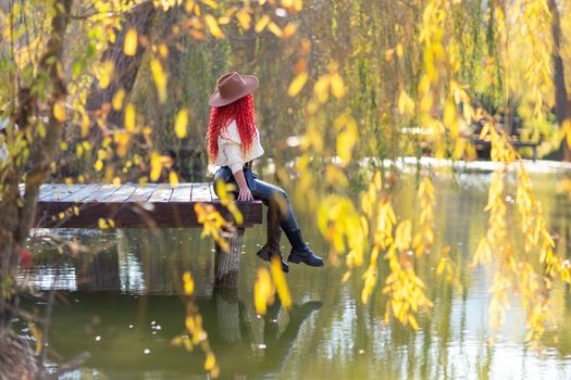 Autumn lake woman. She sits by a pond on a wooden pier in autumn and admires nature. The concept of tourism, weekends outside the city