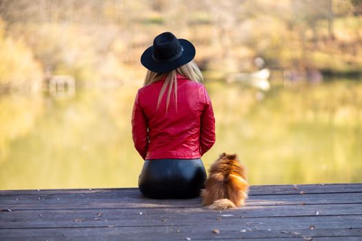 Girl lake autumn dog. A woman sits near a pond in autumn with a spitz dog