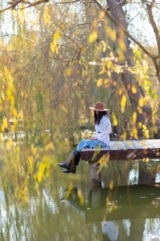 Autumn lake woman. She sits by a pond on a wooden pier in autumn and admires nature. The concept of tourism, weekends outside the city