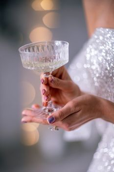 The hands of a woman hold a glass of champagne on a background of golden beke. The concept of the holiday, Christmas, new year, birthday