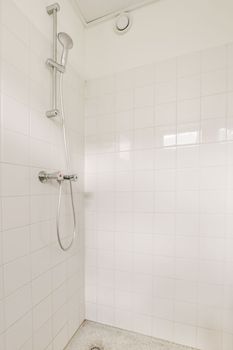 a bathroom with white tiles on the walls and floor, including a shower head mounted in the corner of the bathtub