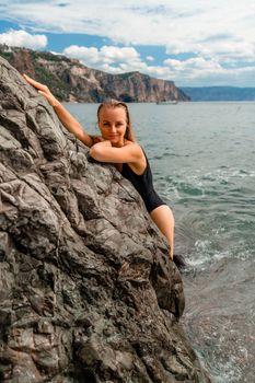 Woman swimsuit sea. Attractive blonde woman in a black swimsuit enjoying the sea air on the seashore around the rocks. Travel and vacation concept