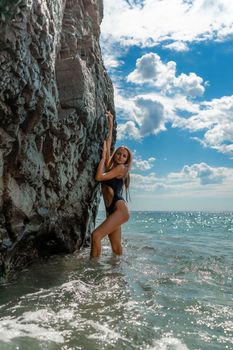 Woman swimsuit sea. Attractive blonde woman in a black swimsuit enjoying the sea air on the seashore around the rocks. Travel and vacation concept