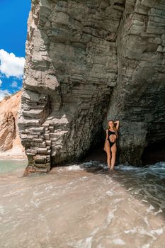 Woman swimsuit sea. Attractive blonde woman in a black swimsuit enjoying the sea air on the seashore around the rocks. Travel and vacation concept