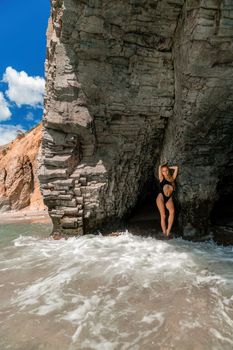 Woman swimsuit sea. Attractive blonde woman in a black swimsuit enjoying the sea air on the seashore around the rocks. Travel and vacation concept