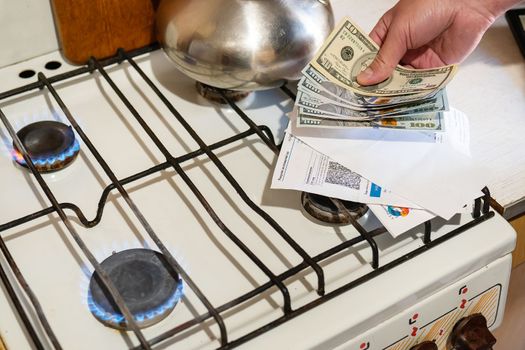 Payment of utility services. Dollar bills, utility bills are held in their hands near a burning gas burner. The concept of increasing the cost of natural gas supply and payment