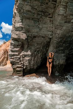 Woman swimsuit sea. Attractive blonde woman in a black swimsuit enjoying the sea air on the seashore around the rocks. Travel and vacation concept