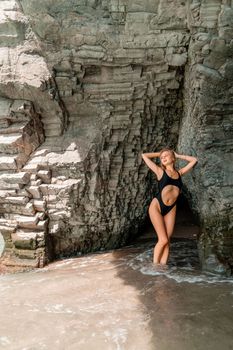 Woman swimsuit sea. Attractive blonde woman in a black swimsuit enjoying the sea air on the seashore around the rocks. Travel and vacation concept