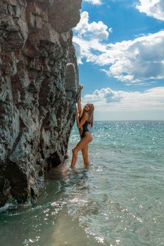 Woman swimsuit sea. Attractive blonde woman in a black swimsuit enjoying the sea air on the seashore around the rocks. Travel and vacation concept