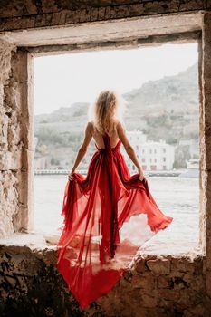 Female redhead model in abandoned building. Fashion Woman in Red fluttering Dress Back Side Rear View.