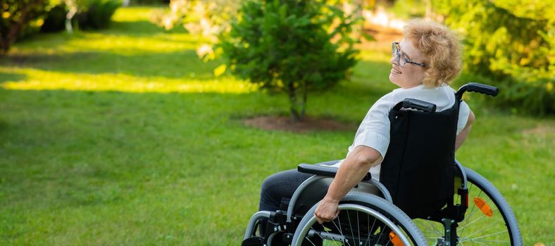 Happy elderly woman sitting in a wheelchair on a walk outdoors