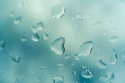 Water drops on glass against blue sky, rainy season concept. Window view background screensaver.