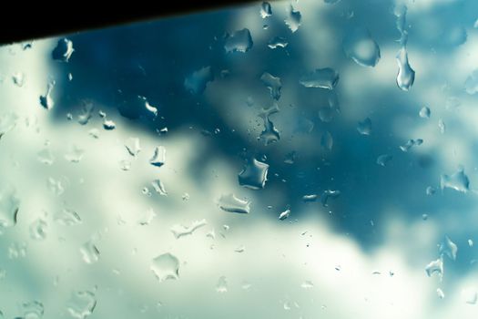 Water drops on glass against blue sky, rainy season concept. Window view background screensaver.