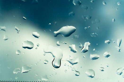 Water drops on glass against blue sky, rainy season concept. Window view background screensaver.