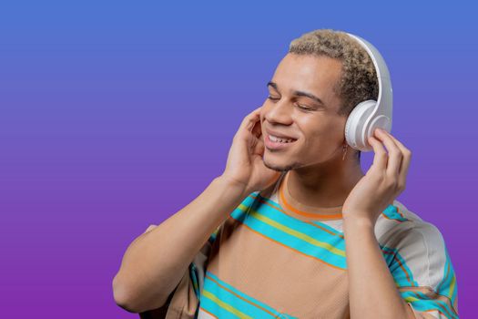 Handsome man listening music, enjoying dance with headphones on violet studio background. Radio, wireless modern sound technology, online player. High quality photo