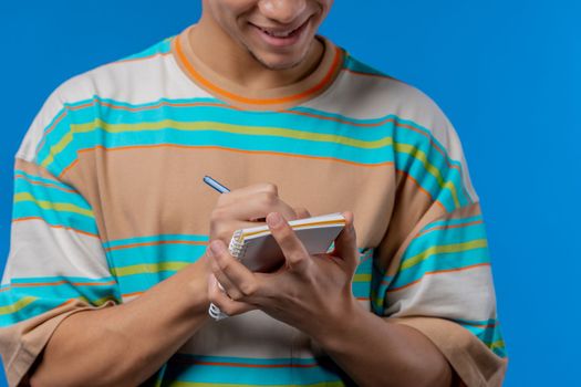 Hands of man writing notes in planner with pen. Student guy writes future plans and to-do list in notebook for week, month, year. Keeping personal diary on blue background. High quality photo