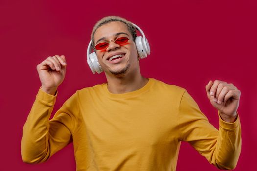Positive man listening music, enjoying dance with headphones on red studio background. Radio, wireless modern sound technology, online player. High quality photo