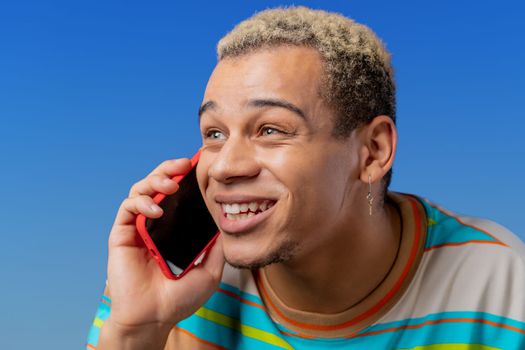 Smiling positive man talking by phone, nice joke, smiling. Young guy on blue background. Having smartphone call. . High quality photo