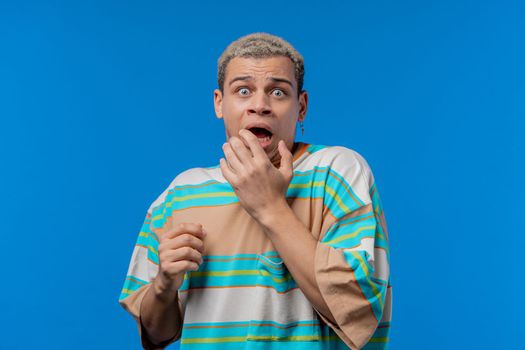 Frightened shocked man afraid of something and looks into camera with big eyes full of horror on blue background. Phobia, trouble, panic concept. High quality photo