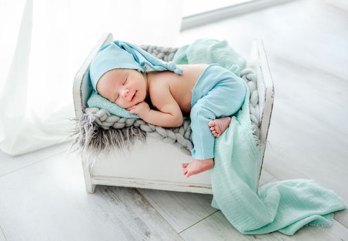 Newborn baby child sleeping on tiny bed on his tommy and wearing knitted pants and hat. Sweet infant kid napping on fur