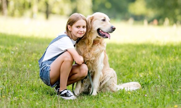 Preteen girl petting golden retriever dog at street. Female child kid with purebred dog labrador sits on ground.