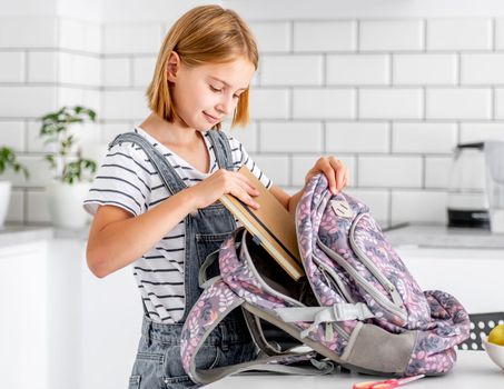 Preteen girl preparing backpack for school class lessons at home and put notebook inside. Female pupil with schoolbag and college supplies