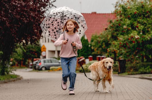 Preteen girl with golden retriever dog running outdoors together. Pretty kid child with purebred pet doggy at street