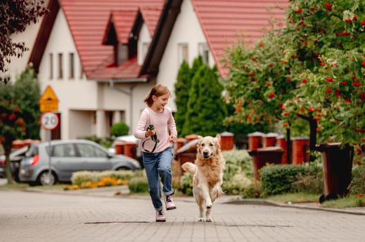 Preteen girl with golden retriever dog running outdoors together. Pretty kid child with purebred pet doggy at street