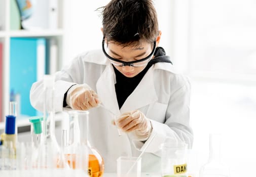 School boy doing chemistry experiment measuring chemical liquids in elementary science class. Clever pupil analyzing results of test in lab