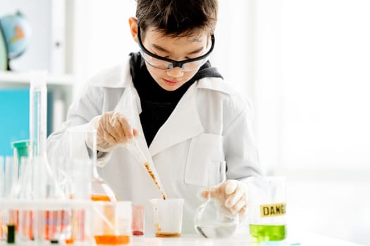 School boy wearing protection glasses with dirty face doing chemistry experiment with chemical liquids in elementary science class. Clever pupil analyzing results of test in lab