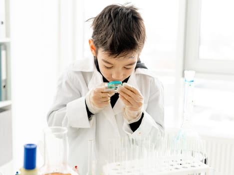 School boy with zoom lens during chemistry experiment in elementary science class. Clever pupil kid in lab