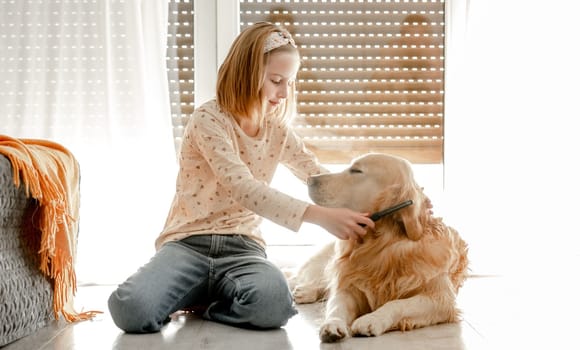 Preteen girl brushes golden retriever dog wet hair after shower and cleaning procedures at home. Pretty child kid with pet labrador friend indoors