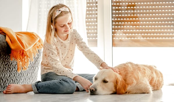 Preteen girl with golden retriever dog lying on floor and smiling. Pretty child kid hugging pet labrador friend indoors