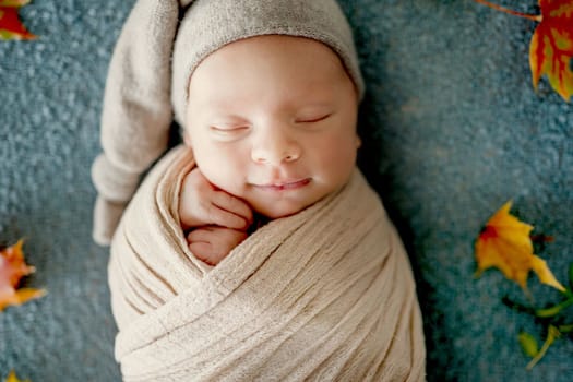 Newborn baby boy swaddled in fabric sleeping with knitted pumpkin toy and decoration. Adorable infant child kid studio halloween portrait