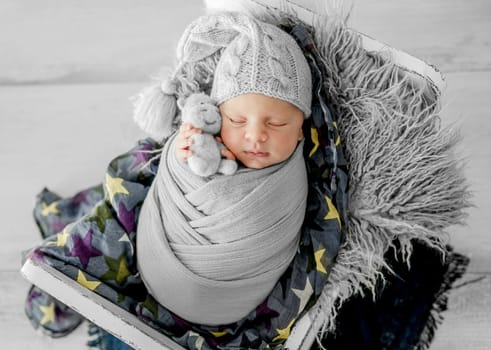 Newborn baby boy sleeping on fur in tiny bed. Adorable infant child kid napping on his tummy during studio photoshoot wearing knitted hat and costume