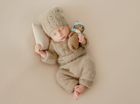 Newborn baby boy sleeping and holding hands under cheeks. Adorable infant child kid napping wearing knitted beige hat and costume