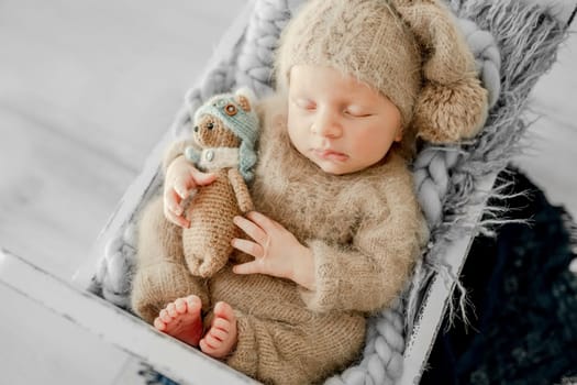 Newborn baby boy sleeping on fur in tiny bed and holding hands under cheeks. Adorable infant child kid napping on his tummy during studio photoshoot wearing knitted hat and costume