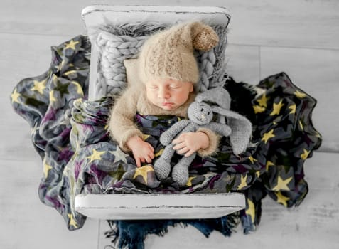 Newborn baby boy sleeping on fur in tiny bed. Adorable infant child kid napping on his tummy during studio photoshoot wearing knitted hat and costume