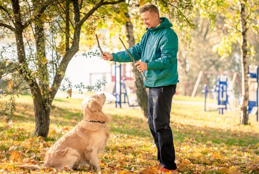 Man playing with his dog golden retriever in autumn park