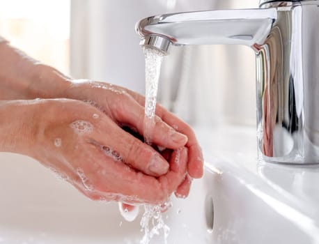 Young woman washes her hands with soap over the sink in the bathroom, close-up.